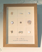 A wooden frame displaying nine pearls in a three-by-three arrangement, with a handwritten message beneath them.