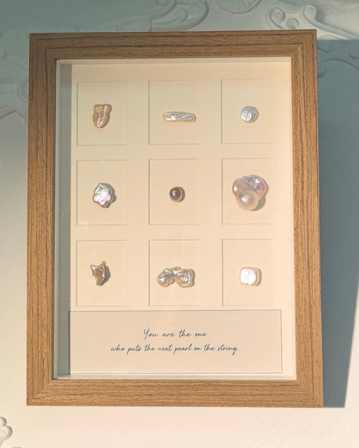 A wooden frame displaying nine pearls in a three-by-three arrangement, with a handwritten message beneath them.