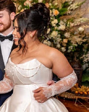 A bride in a white wedding gown, with pearl strands draped in soft arcs across the bodice.