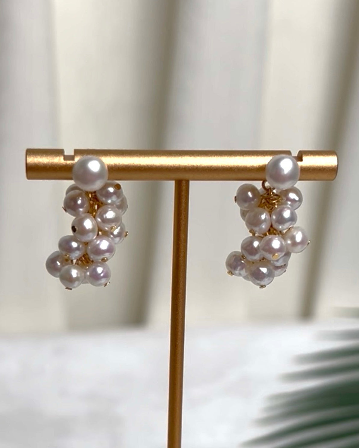 A pair of pearl cluster earrings on a display stand, each with a larger round pearl above a cluster of smaller pearls.