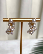 A pair of pearl cluster earrings on a display stand, each with a larger round pearl above a cluster of smaller pearls.