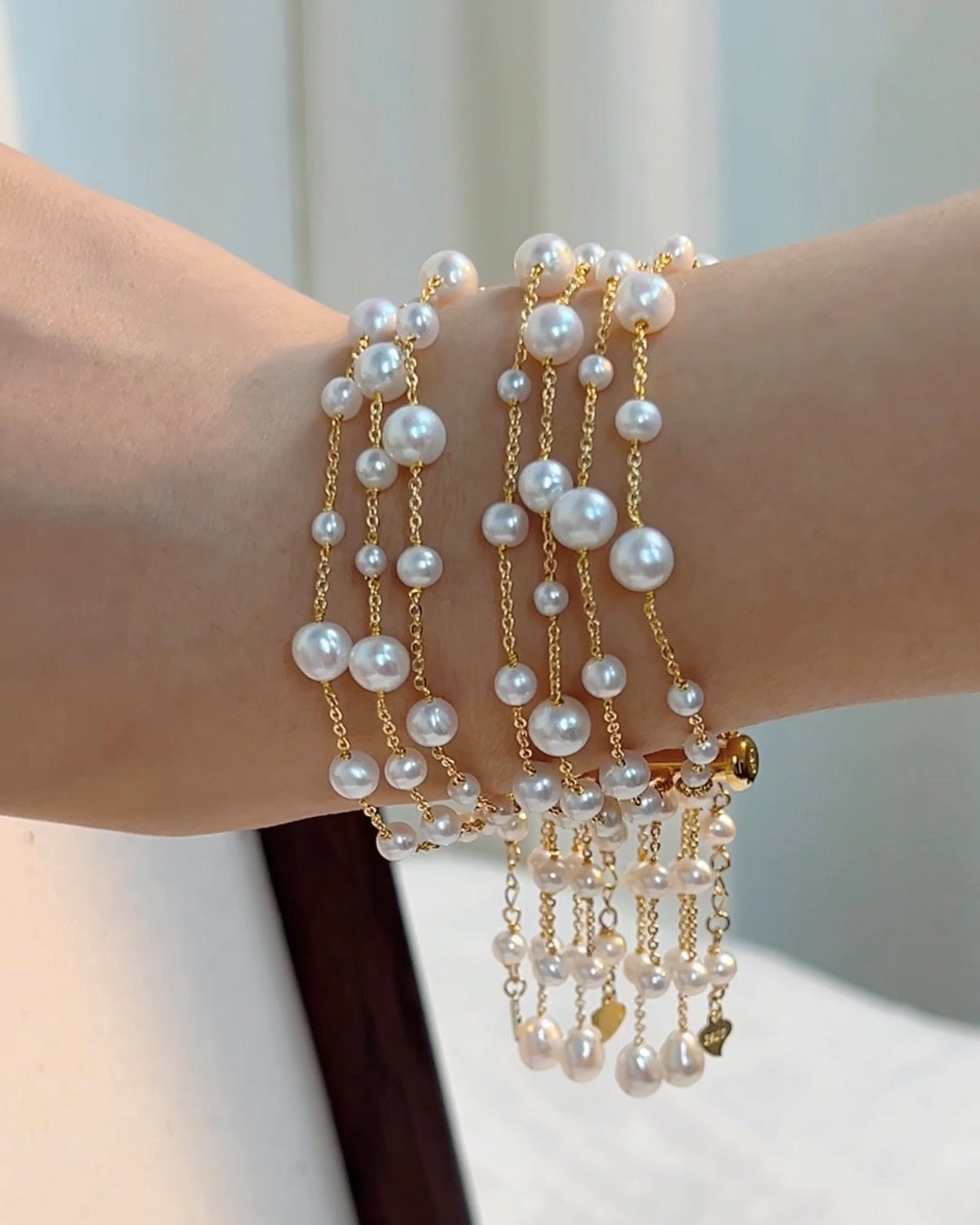 A close-up of a multi-strand pearl bracelet on the wrist, with pearls of varied sizes along fine gold-tone chains and pearl strands hanging below.