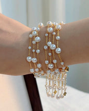 A close-up of a multi-strand pearl bracelet on the wrist, with pearls of varied sizes along fine gold-tone chains and pearl strands hanging below.