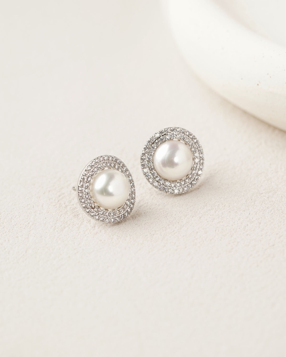 Aurora pearl stud earrings with sparkling halos on a pale textured surface.