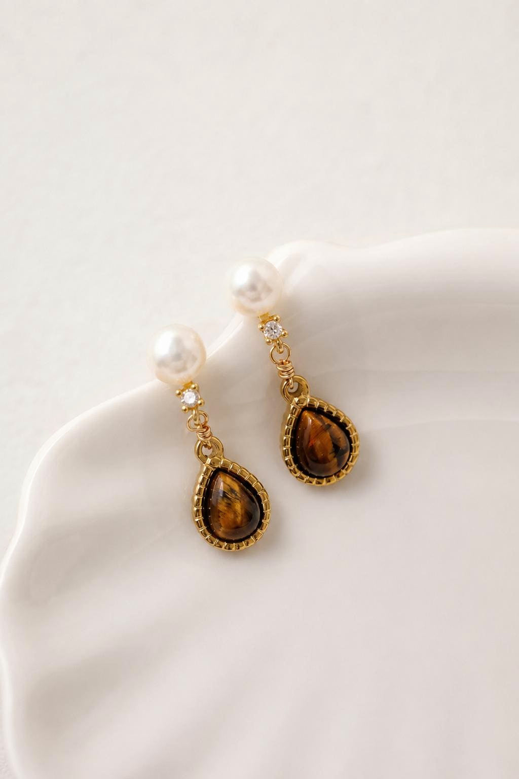 Valour Earrings with white pearls and brown teardrop accents on a pale dish; styling example, not a same-scale size comparison.