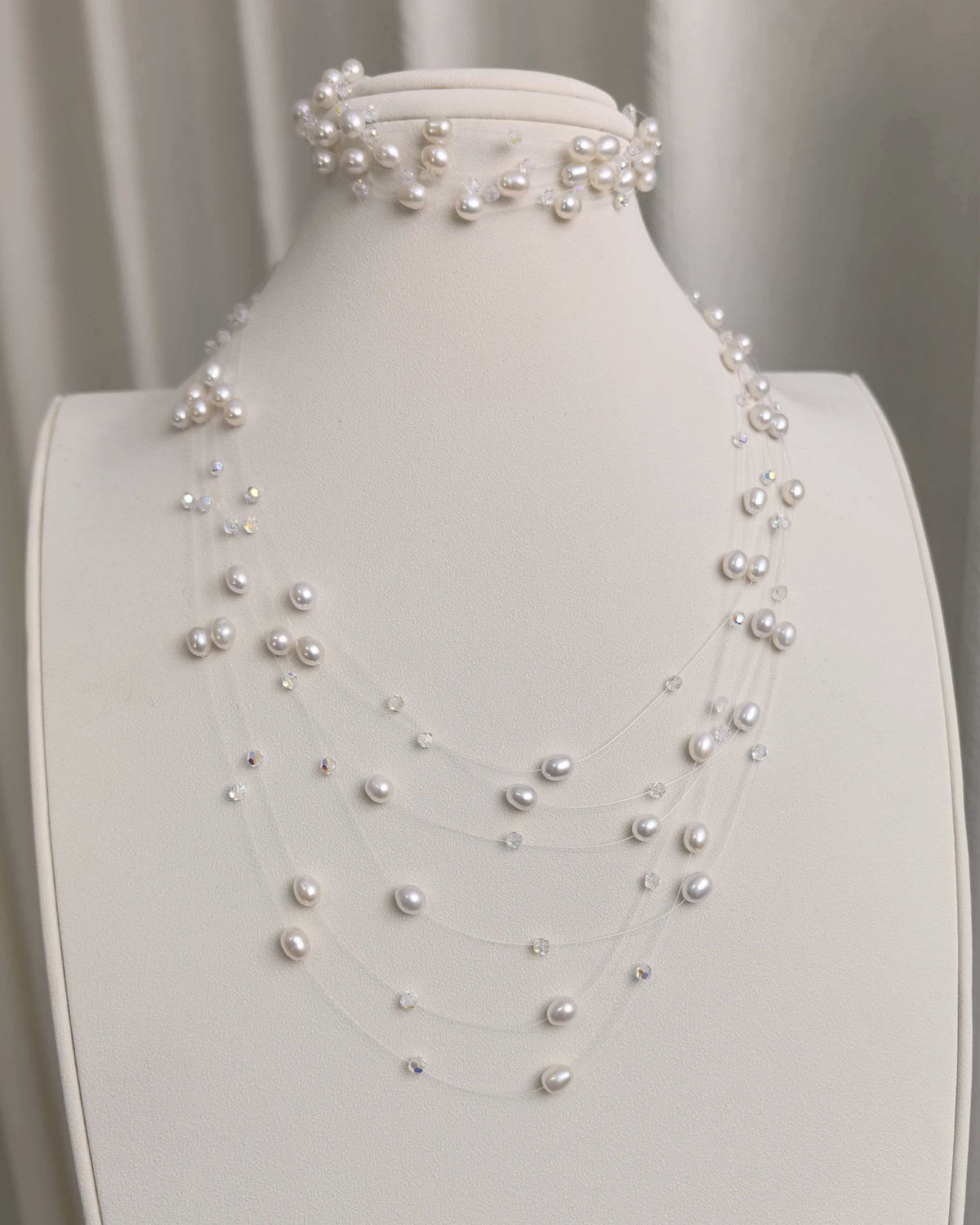 A layered floating pearl necklace with small crystals, displayed with a matching interlaced pearl bracelet.