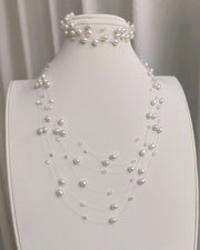 A layered floating pearl necklace with small crystals, displayed with a matching interlaced pearl bracelet.