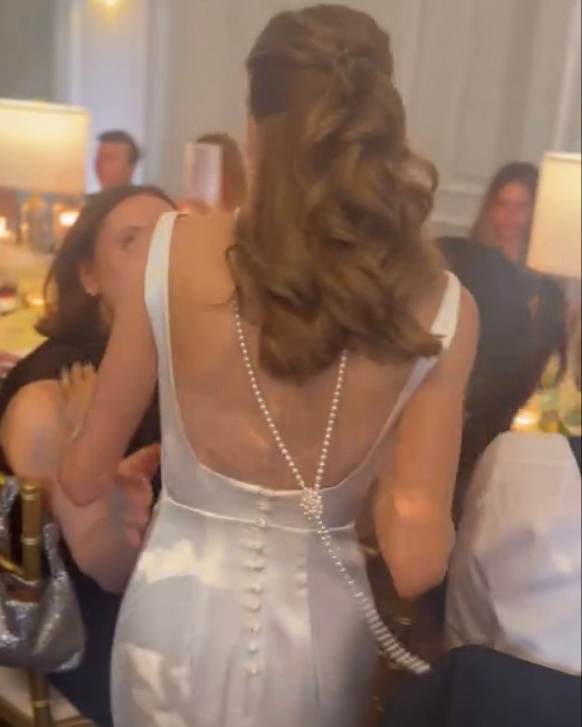 A bride seen from behind in an open-back wedding dress, with pearls draped down her back and tied into a long trailing detail.